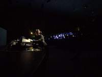 In a dark space, a person stands behind a control desk.