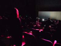 People take their seats in a dark auditorium.
