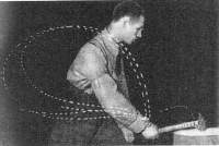 A black-and-white photograph shows a male presenting person chopping wood with a hammer. There are white dotted lines on the photograph, which collide in the person's hand.