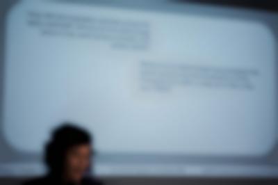 A person's head appears in front of a powerpoint slide projection. The white slide asks two questions about how the usage of photography and video throughout the twentieth century, which appear in black.