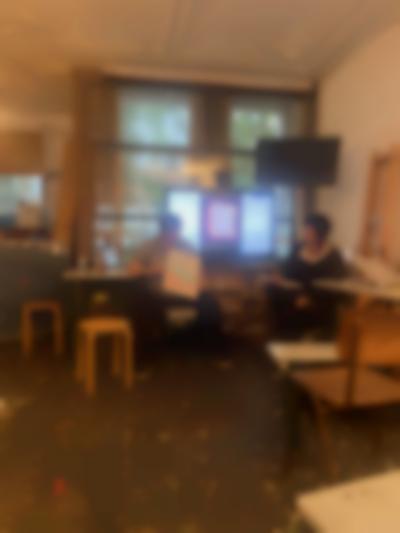 Two people are having a discussion in front of a screen showing an image. One of them is holding a poster, which the other person looks towards.