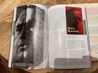 A book has been left open on a table. There is a photograph on the left page and a text on the right. A small image on the right hand page says 