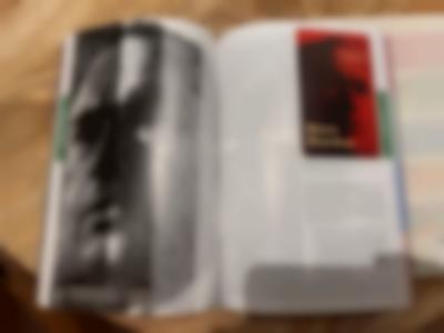 A book has been left open on a table. There is a photograph on the left page and a text on the right. A small image on the right hand page says 