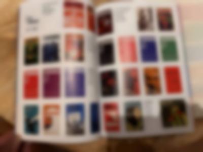 A hand is holding a book open, showing two pages with several posters.