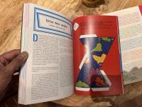 A hand is holding a book open. On the left page, there is a text written in French. There is an image on the right page.