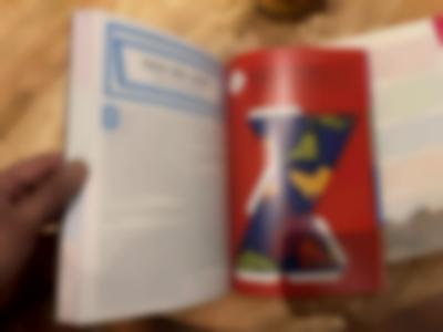 A hand is holding a book open. On the left page, there is a text written in French. There is an image on the right page.