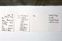 Four white A4 sheets, with Dutch words handwritten in black ink, are stuck to a wall.