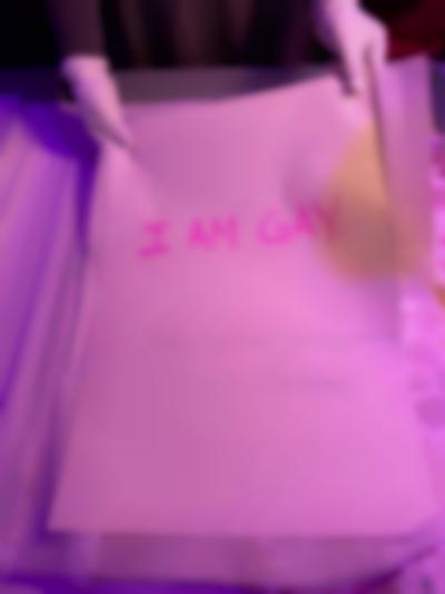 Two hands, wearing white gloves, hold a large white sheet of paper, which reads 