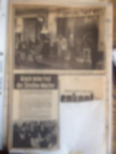 Collage made from a newspaper page. Half of the page is occupied by a photograph depicting a group of people standing in front of a storefront. At the bottom half, there's an article with a photo and a missing chunk, on top of which there's a cut out from a different page, which only partially occupies the missing space.