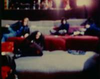 In a blurry image, four people lie down in two levels of sofa-like seating. The face of a fifth person is visible on the bottom left corner.