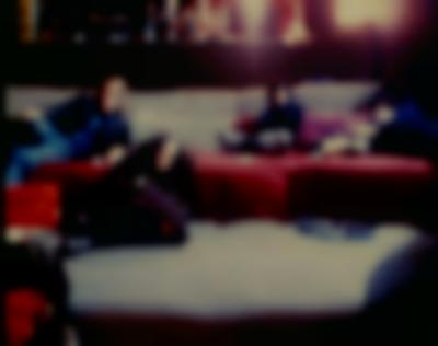 In a blurry image, four people lie down in two levels of sofa-like seating. The face of a fifth person is visible on the bottom left corner.