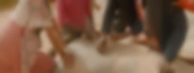 Hands, arms and torsos of a group of four people. They are sitting around a rock, where they are placing small rocks on top of a square one of them is drawing.