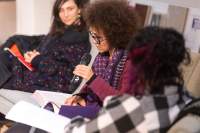 A person is reading from a book, holding the microphone. Two people, one on each side, look towards the person with the microphone.