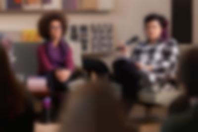 Two people sit next to each other on a stage. Megan speaks into the microphone. At the front, slightly blurred, three people face the stage.