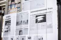 Close-up of a large screen. The installation is made from several A4 sheets attached to each other with metal rings. There are large scans of newspaper articles printed across these pages.