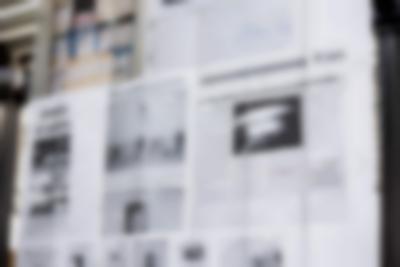 Close-up of a large screen. The installation is made from several A4 sheets attached to each other with metal rings. There are large scans of newspaper articles printed across these pages.