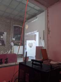 On the other side of a glass, an image is being projected in one of the walls of a gallery space. Above the image with a drawing of a face, text white reads: 