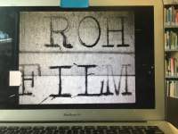A film still appears in a grey laptop screen. The black and white still reads 