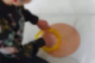 A coil spiral has been stuck to the white floor with a transparent plastic. There are two cables attached to it, one to the centre and the other to the edge. A person can partially be seen sitting next to it. With their left hand they are holding a small yellow heptagon structure against the spiral. With their right hand, they are touching the spiral through the middle of the structure.