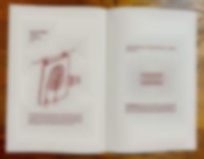 A booklet lies open, showing two white pages, each with some text and a line illustration, in dark red. On the left page the title reads: