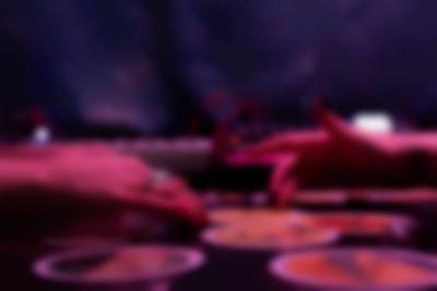 Two hands, belonging to two people sitting across from each other, are touching the same tarot card. Around it, there are other cards.