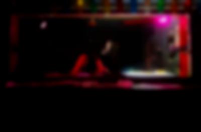 A person stands in a dark DJ booth, adjusting the knobs on a DJ deck. To their right, a bright light shines upwards from a light box that is set next to the deck.