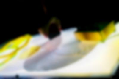 On top of a light box, there are two coil spirals and a small sound deck with knobs. A hand can be seen holding an object, placed on top of one of the spirals.