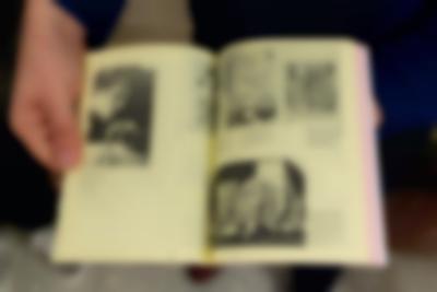 A book is held open, showing a spread with yellow pages and four different images with descriptions. In the most visible them, a person uses a compass.