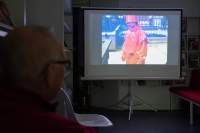 A person looks towards a pull down projector, where a film is being projected. The image shows a person in a full orange suit and hat.