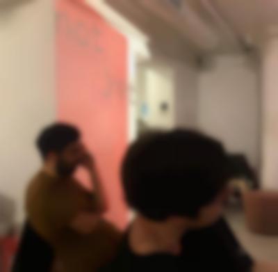 Two people are sitting, facing the same direction. Behind them, there is wall projection of a red block with the words 