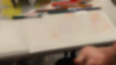 A white sheet of paper with notes and drawings is at the edge of a table. There are pens and pencils around it. The hand of the person sitting in front of the sheet can be see on the bottom right corner.