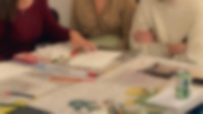 Several sheets with handwritten notes, printouts with notes and a photograph have been laid on a table. There are also pens and pencils, a glass and a can of beer. Three people are partially visible around the table, one of them has their hand on top of one of the sheets.