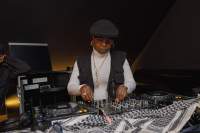 A person is behind the decks, which they are adjusting. A black and white keffiyeh lays in front of the decks.