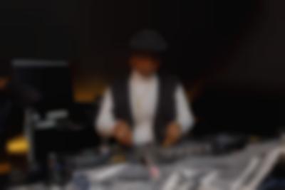 A person is behind the decks, which they are adjusting. A black and white keffiyeh lays in front of the decks.