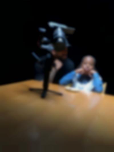 A child and an adult person sit at a table. In front of them, a camera on a gimbal has been left on the table.