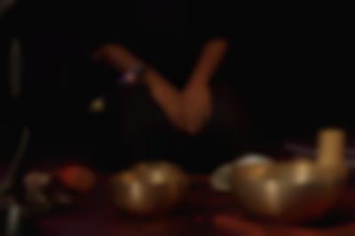 Three singing bowls have been set on a surface, below a microphone. Behind them, someone sits on their heels, with their hands on their knees.